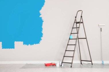 Dekoratör aletleri ve odanın zeminine boya. Duvar kısmen açık mavi renge boyanmış. İç yenileme