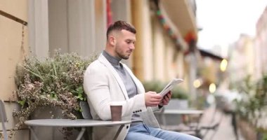 Genç adam açık kafedeki masada gazete okuyor.