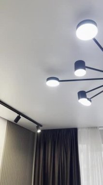 Aydınlatılmış bir avize ve odanın beyaz tavanında raylı aydınlatma.