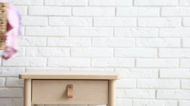 Çamaşır sepetini ve elbiselerini beyaz tuğla duvarın yanındaki masaya koyan kadın, yakın plan.