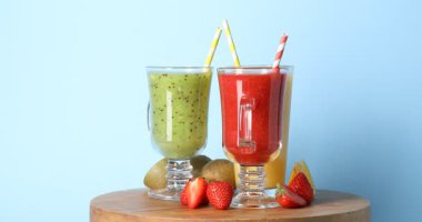 Açık mavi arka planda dönen bardaklar ve malzemelerle farklı lezzetli içecekler, yakın plan