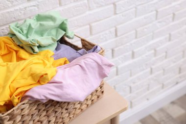 Çamaşır sepetinin içinde beyaz tuğla duvarın yanındaki masada giysiler var. Yakın plan. Metin için boşluk