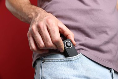 Kırmızı arka planda cebinde gizli casus kamerası olan adam, yakın plan.