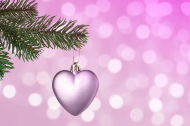 Pembe arka plandaki bulanık ışıklara karşı kalp şeklinde süslemeleri olan Noel ağacı dalı