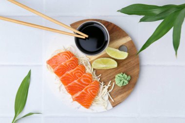 Dilimlenmiş turplu taze somon balığı, wasabi, limon ve soya sosu açık fayanslı masada, düz yatıyordu.