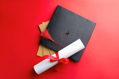 Diploma, not defteri ve kırmızı arka planda mezuniyet şapkası.
