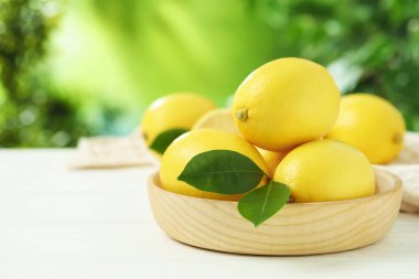 Beyaz ahşap masa üzerinde yeşil yapraklı taze limonlar, yakın plan. Metin için boşluk