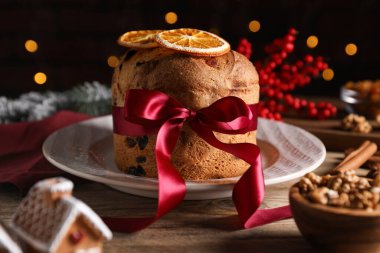 Noel yemeği. Lezzetli Panettone pastası, malzemeler ve ahşap masanın üzerindeki dekoratif dekor arka planda bulanık ışıklar, yakın plan. Bokeh etkisi