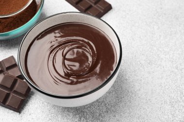 Erimiş çikolata kasede, parçalar ve açık gri masada kakao tozu, yakın plan. Metin için boşluk