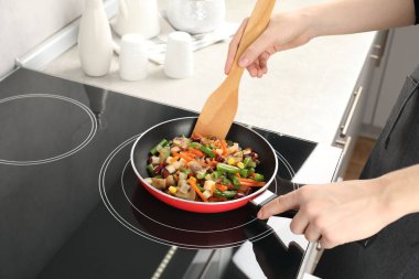 Kızartma tavasında taze sebze ve ahşap spatula karıştıran kadın, yakın plan.