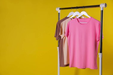 Farklı kadın kıyafetleri sarı arka planda asılı duruyor. Metin için boşluk