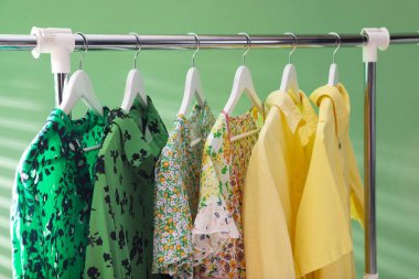 Farklı kadın kıyafetleri yeşil arka planda asılı, yakın plan.