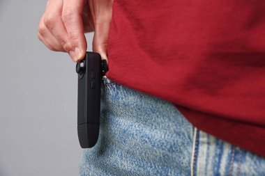 Cebinde gizli kamera olan genç bir kadın açık gri arka planda, yakın plan.