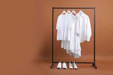 Askıda asılı farklı kıyafetler ve kahverengi arka planda ayakkabılar, metin için boşluk