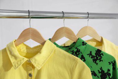 Beyaz duvarın yanında askıda asılı farklı şık kıyafetler, yakın plan.