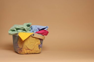 Açık kahverengi arka planda giysileri olan çamaşır sepeti. Metin için boşluk