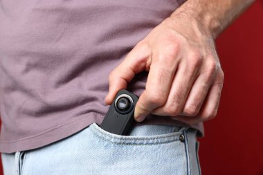 Kırmızı arka planda cebinde gizli casus kamerası olan adam, yakın plan.