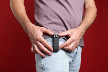 Kırmızı arka planda cebinde gizli casus kamerası olan adam, yakın plan.