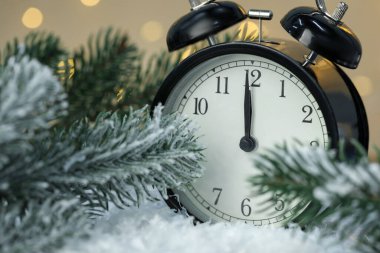 Alarm saati ve köknar ağacı dalları suni kar üzerinde altın arka planda bulanık ışıklarla, yakın plan. Yeni yıl tebrik kartı.
