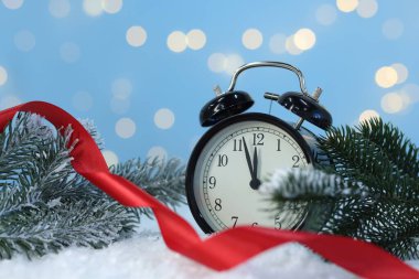 Alarm saati, kurdele ve köknar ağacı dalları yapay kar üzerinde açık mavi arka planda bulanık ışıklarla, yakın plan. Yeni yıl tebrik kartı.