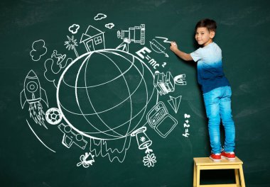 Yeşil tahtaya tebeşirle çizen küçük çocuk.