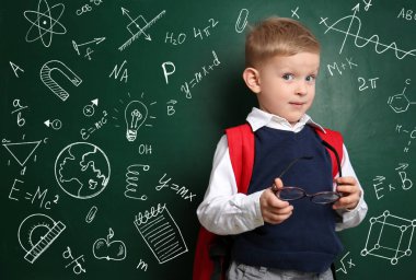 Yeşil karatahtanın yanında formülleri ve çizimleri olan sevimli küçük bir çocuk.