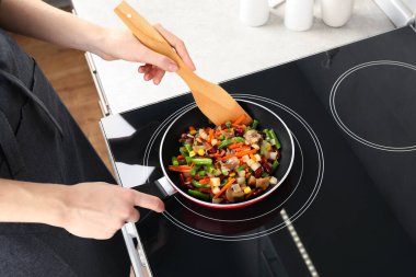 Kızartma tavasında ahşap spatulayla taze sebzeleri karıştıran kadın.