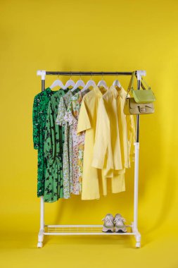 Farklı kadın kıyafetleri sarı arka planda asılı duruyor.