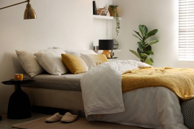 Yatak odasındaki beyaz duvarın yanında çarşafları, komodinleri ve lambaları olan büyük bir yatak.