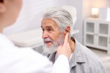 Doktor hastanede yaşlı adamın kulağına işitme cihazı takıyor.