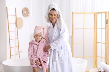 Anne ve kız göz bantlı ve banyoda bornoz giyen saçları sarılı.