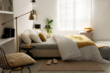 Yatak odasının penceresinin yanında çarşafları ve pufları olan büyük bir yatak.