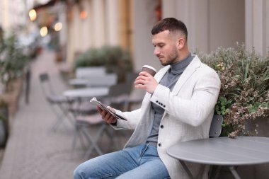 Genç adam açık kafede kahve içerken gazete okuyor. Metin için boşluk