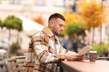 Genç adam açık kafedeki masada gazete okuyor.
