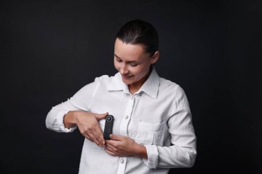 Siyah arka planda cebinde gizli kamera olan genç bir kadın.