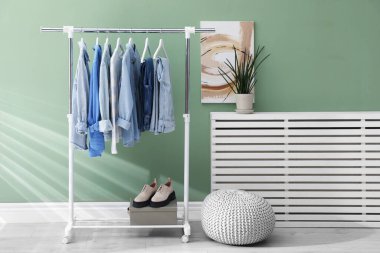 İçerideki yeşil duvarın yanında askıda asılı farklı şık elbiseler, puf ve bitkiler.