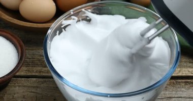 Tahta masada el çırpıcı ile yumurta beyazı çırpmak, yakın plan.