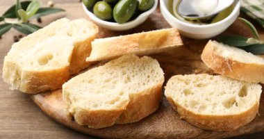 Ciabatta dilimlerinin üzerine tahta masada kaşıkla yağ dök, yakın plan.