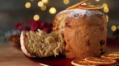 Noel yemeği. Lezzetli Panettone pastası ve ahşap masanın üzerindeki şenlikli dekor. Arka planda bulanık ışıklar, yakın plan. Kamera sağa hareket ediyor