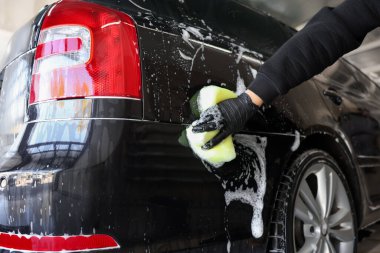 Oto yıkayan adam araba yıkamada süngerle yıkıyor.