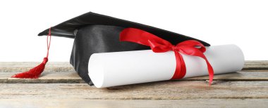 Diploma ve mezuniyet şapkası beyaz arka plana karşı ahşap masada.