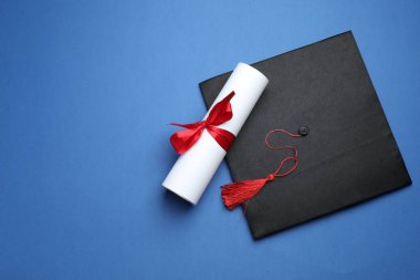 Mavi arka planda diploma ve mezuniyet şapkası, üst manzara. Metin için boşluk