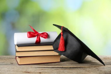 Diploma, mezuniyet şapkası ve ahşap masa üzerindeki kitap yığını bulanık arka plan, yakın plan