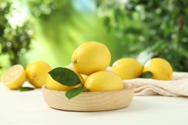 Beyaz ahşap masa üzerinde yeşil yapraklı taze limonlar, yakın plan.