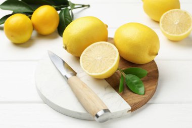 Yeşil yapraklı taze limonlar ve beyaz ahşap masada bıçak, yakın plan.