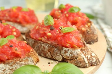 Domatesli lezzetli bruschettalar ve beyaz masada fesleğen, yakın plan.