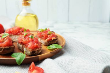 Domatesli lezzetli bruschettalar ve beyaz masada fesleğen, yakın plan. Metin için boşluk