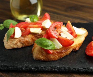 Mozarella peynirli, domatesli ve ahşap masadaki fesleğenli lezzetli bruschettalar.