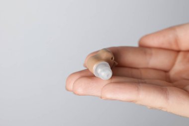 Açık gri arka planda işitme cihazı olan bir kadın, yakın plan. Metin için boşluk