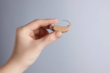 Açık gri arka planda işitme cihazı olan bir kadın, yakın plan. Metin için boşluk